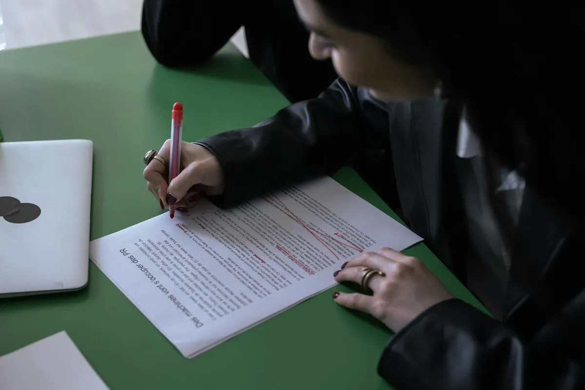 A manuscript being edited with a red pen on a study desk